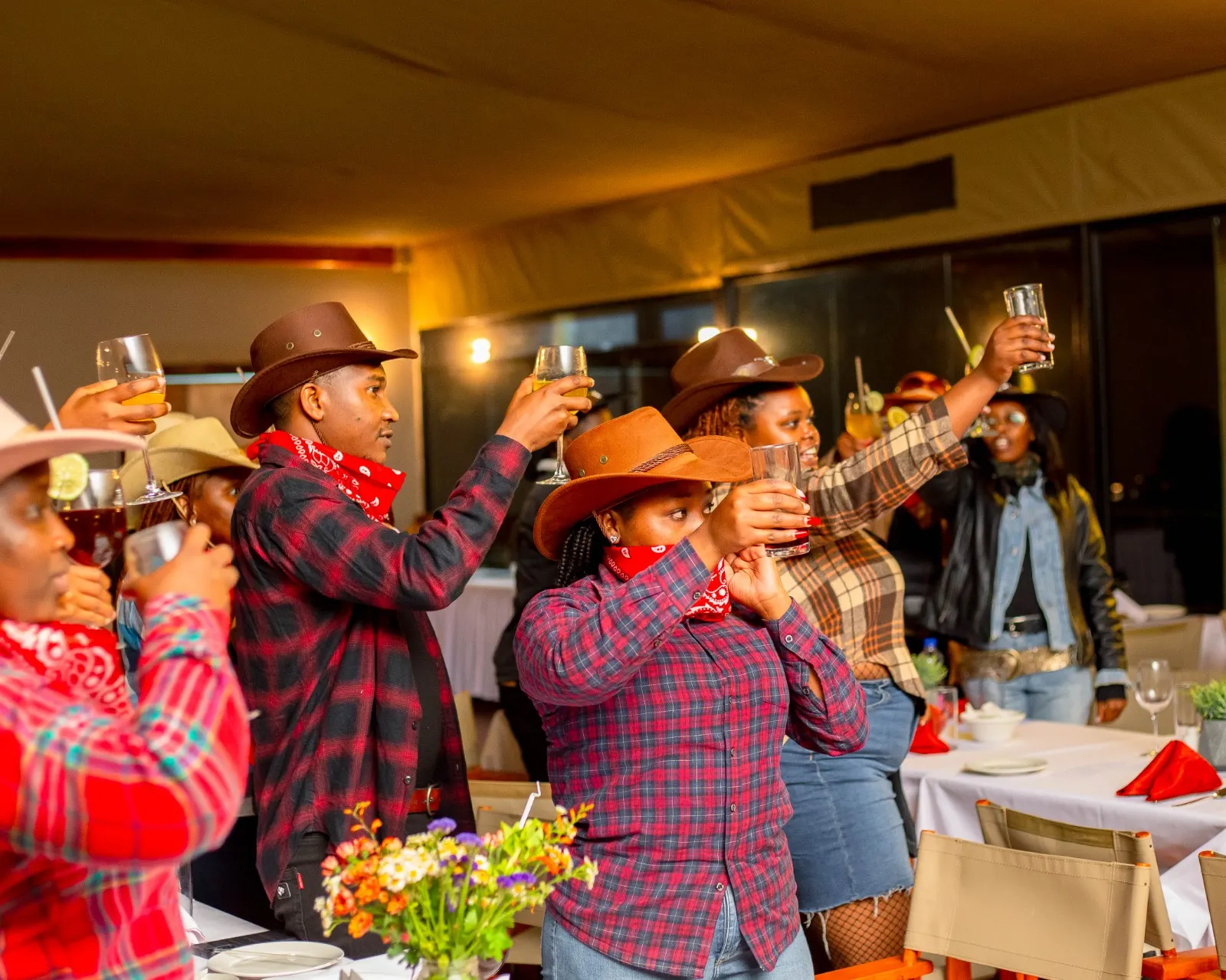 Guests in cowboy hats raising a toast at a themed dinner night at Mtalii Bush Camps