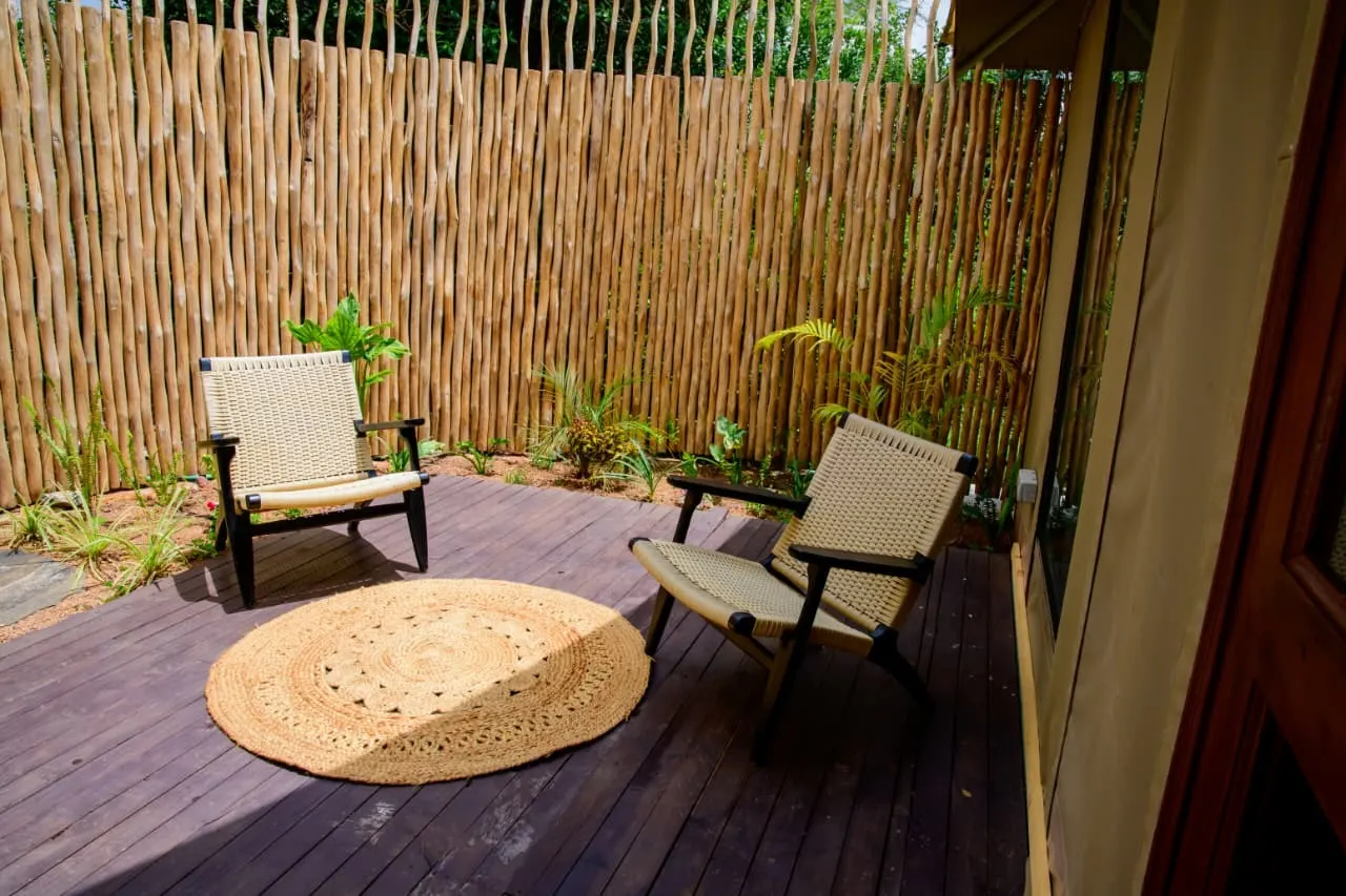 A private timber deck with woven chairs, screened by a bush garden, at a Mtalii tented suite